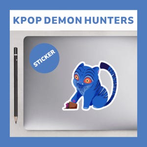 Peut inclure: Un autocollant bleu représentant une créature ressemblant à un tigre de dessin animé avec des yeux orange et des rayures. L'autocollant est sur un ordinateur portable, avec le texte "KPOP DEMON HUNTERS" au-dessus et un cercle bleu avec "STICKER".