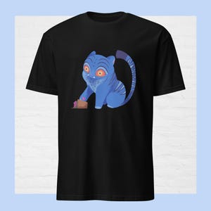 Peut inclure: T-shirt noir avec un dessin d'une créature bleue ressemblant à un tigre, avec des yeux oranges et des rayures. La créature tient un petit objet marron. Le t-shirt est fait d'une matière douce.