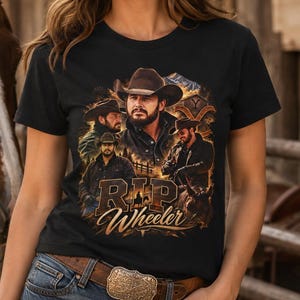May include: A black short-sleeved t-shirt featuring a graphic print of a man in a cowboy hat, with the text "RIP Wheeler" in a bold, distressed font. The design includes multiple depictions of the same figure in various poses and settings.