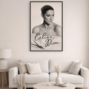 Puede incluir: Impresión en blanco y negro enmarcada con un retrato de Celine Dion. La imagen muestra su rostro y hombros, con el texto "Celine Dion" en cursiva. La impresión está colgada sobre un sofá blanco.
