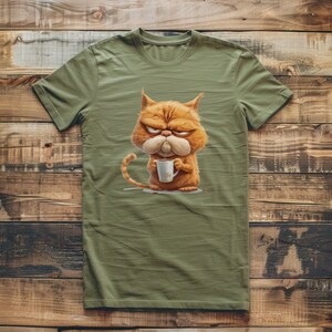 Op de afbeelding: Een groen T-shirt met een cartoonillustratie van een oranje kat met een chagrijnige uitdrukking die een kopje koffie vasthoudt.