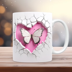 May include: White ceramic mug with a butterfly design. The design features a white butterfly with black detailing set against a pink heart shape, framed by a cracked white surface. The mug has a white handle.