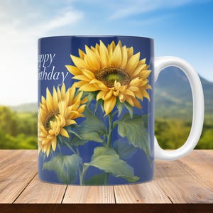Può includere: Tazza con manico bianco con un disegno di due girasoli gialli su sfondo blu scuro. Le parole "Happy Birthday" sono stampate sulla tazza. La tazza è appoggiata su una superficie di legno.