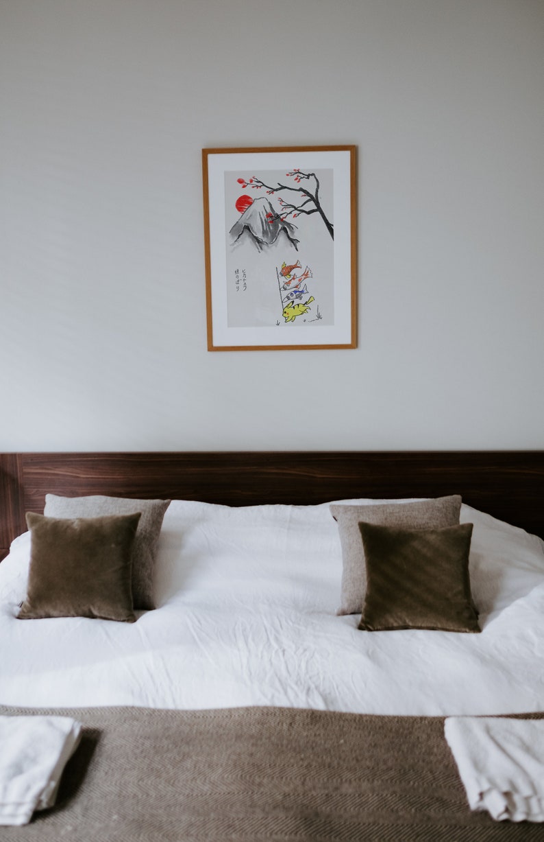 K&ouml;nnte beinhalten: Ein wei&szlig;es Bett mit einem braunen Kopfteil und einer braunen Decke. Auf dem Bett liegen zwei braune Kissen und zwei beige Kissen. &Uuml;ber dem Bett h&auml;ngt ein gerahmter Druck einer Bergszene mit einer roten Sonne und Fischen.