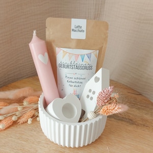 Könnte beinhalten: Eine weiße, geriffelte Schale enthält eine rosa Kerze mit Herz, ein weißes herzförmiges Objekt, ein kleines weißes Haus, Trockenblumen und eine Packung mit der Aufschrift "Latte Macchiato". Eine Karte trägt die Aufschrift "ein kleiner GEBURTSTAGSGRUSS" mit einer Geburtstagsbotschaft.