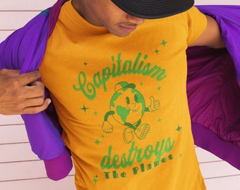 May include: A yellow t-shirt with a green cartoon earth character and the text "Capitalism destroys the planet". The person is wearing a purple jacket and a black baseball cap.