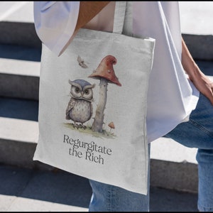 May include: A white canvas tote bag with a brown owl and a red mushroom illustration. The text "Regurgitate the Rich" is printed on the bag.