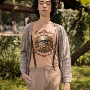 May include: A person wearing a brown cardigan over a light brown t-shirt with a skull and floral design and the text "Dead Inside, Ready to Burn It All". The person is also wearing brown pants with suspenders.