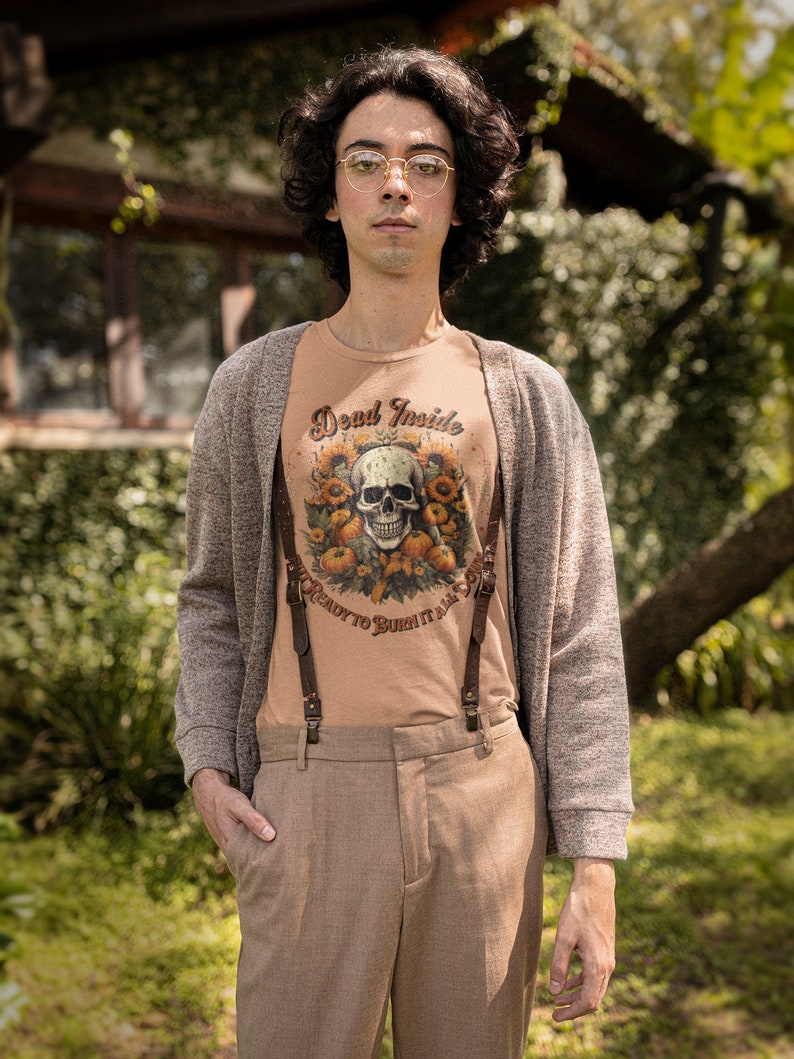 May include: A person wearing a brown cardigan over a light brown t-shirt with a skull and floral design and the text "Dead Inside, Ready to Burn It All". The person is also wearing brown pants with suspenders.