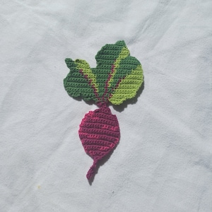 May include: A handmade crochet radish applique. The radish is a deep magenta color, with a green and yellow-green leafy top. The applique is likely for clothing or craft projects.