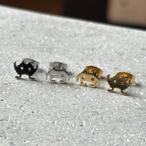 Könnte beinhalten: Vier silberne und goldene Ohrringe in Alienform. Die Ohrringe sind klein und haben ein detailliertes Design.