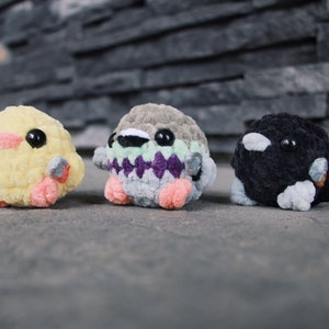 May include: Three crocheted stuffed animals, a yellow duck, a gray and purple bird, and a black and white penguin.