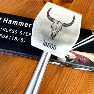 May include: A silver meat mallet with a skull design and the name "Jason" engraved on the head. The mallet is made of stainless steel and has a long handle.