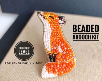 Könnte beinhalten: Ein besticktes Fuchsanstecknadel-Set mit orangefarbenen, weißen und schwarzen Perlen. Der Fuchs blickt nach oben. Der Text "BEADED BROOCH KIT" ist zu sehen. Das Set ist mit "BEGINNER LEVEL" gekennzeichnet und enthält ein PDF (Englisch) und ein Video.