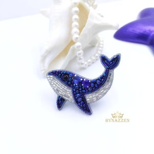 Op de afbeelding: Een blauwe en witte walvis broche gemaakt van kralen. De walvis kijkt naar rechts en heeft een witte buik en een blauwe rug. De broche is een handgemaakt sieraad.