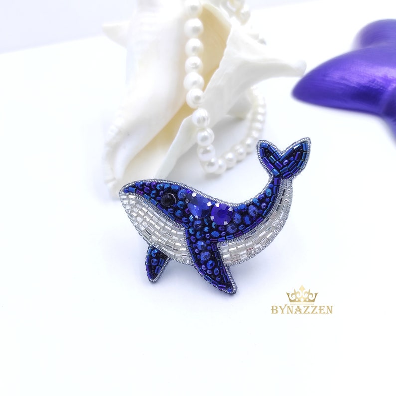 Op de afbeelding: Een blauwe en witte walvis broche gemaakt van kralen. De walvis kijkt naar rechts en heeft een witte buik en een blauwe rug. De broche is een handgemaakt sieraad.