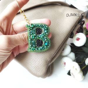 May include: A green and black beaded letter B keychain. The letter is made of small green and black beads and is attached to a gold chain.