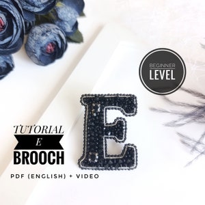 May include: A black beaded letter E brooch, a beginner level craft project. The image includes the text "TUTORIAL E BROOCH PDF (ENGLISH) + VIDEO" and "BEGINNER LEVEL".