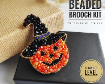 Könnte beinhalten: Ein Perlenbroschen-Set mit einem Halloween-Kürbismotiv. Der Kürbis ist orange mit einem schwarzen Hexenhut, und die Brosche ist mit Perlen verziert. Der Text auf dem Bild lautet "Beaded Brooch Kit" und "Beginner Level".