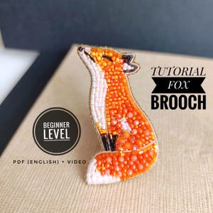 May include: A beaded fox brooch in shades of orange, white, and black. The brooch is made with small beads and has a detailed design. The text "Tutorial Fox Brooch" is displayed above the brooch, and "Beginner Level" is displayed below.