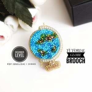 Könnte beinhalten: Eine Anleitung für eine Perlen-Globus-Brosche für Anfänger. Das Tutorial beinhaltet ein PDF in englischer Sprache und ein Video. Die Brosche ist aus blauen, grünen und braunen Perlen gefertigt und hat eine goldene Basis.