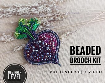 Könnte beinhalten: Ein Perlenstickerei-Set für eine Brosche in Form einer Roten Bete, gefertigt aus dunkelvioletten und roten Facettenperlen mit hellgrünen Paillettenblättern. Der Text lautet BEADED BROOCH KIT, BEGINNER LEVEL und PDF (ENGLISH) + VIDEO.