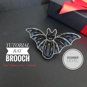 May include: A black bat brooch with intricate bead and sequin detailing. The brooch features a silver wire outline and accents of blue sequins. Text on the image reads "Tutorial Bat Brooch" and "Beginner Level".