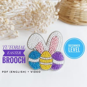 May include: A beaded Easter egg brooch with bunny ears. The eggs are blue, yellow, and purple. The bunny ears are white with pink accents. The brooch is a beginner level craft project. The text "TUTORIAL EASTER BROOCH" is at the top of the image. The text "PDF (ENGLISH) + VIDEO" is at the bottom of the image. The text "BEGINNER LEVEL" is in a blue circle.