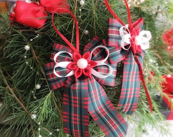 Könnte beinhalten: Weihnachtsschmuck mit rot-weiß-grünen karierten Schleifen. Jede Schleife hat eine rot-weiße Blume mit einem Perlenmittelpunkt. Die Ornamente hängen an grünen Tannennadeln, mit weißen Perlenschnüren.