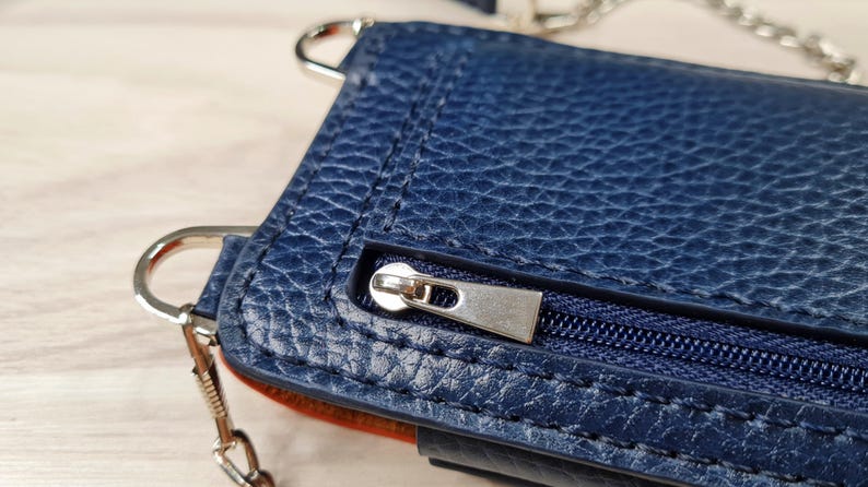 May include: A dark blue leather purse with a silver zipper and a silver chain strap.