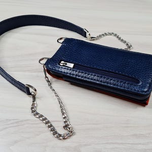 May include: A blue leather crossbody phone bag with a silver chain strap. The bag has a zippered pocket and a flap closure.