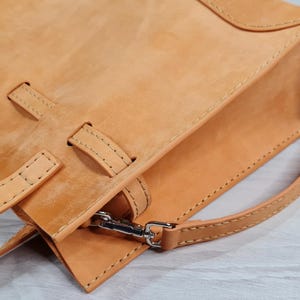 May include: A tan leather tote bag with a top handle and a shoulder strap. The bag has a flap closure and a decorative stitching detail.