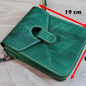 Może przedstawiać: Zielona sk&oacute;rzana torba na ramię z klapką i paskiem. Torba ma około 19 cm szerokości i 16 cm wysokości. Posiada okrągły otw&oacute;r na klapie i białe przeszycia. Torba wykonana jest z teksturowanej sk&oacute;ry.