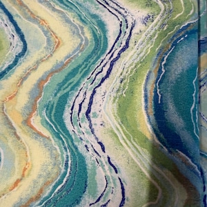 May include: Close-up of a fabric with a swirling, abstract pattern. The design features flowing lines in shades of blue, green, yellow, and white, creating a marbled effect. The fabric's texture is visible, suggesting a soft material.