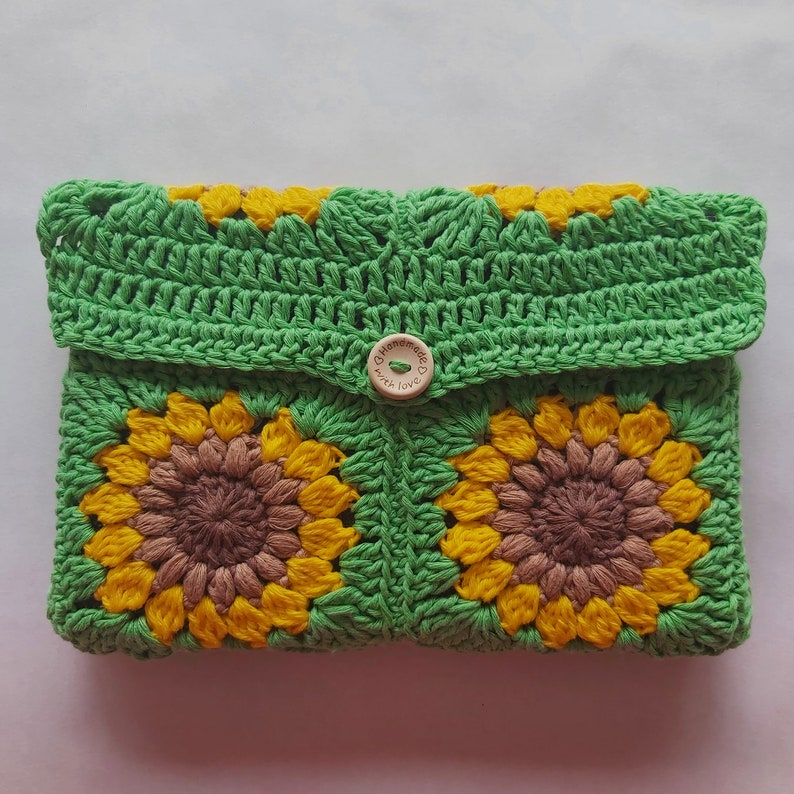 May include: Green crocheted clutch with two brown and yellow sunflower designs and a wooden button that says "Handmade with love".