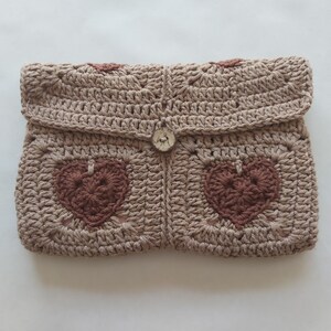May include: A beige crocheted clutch with a brown heart design and a white button closure.