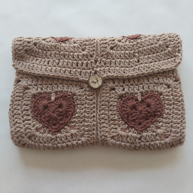 May include: A beige crocheted clutch with a brown heart design and a white button closure.
