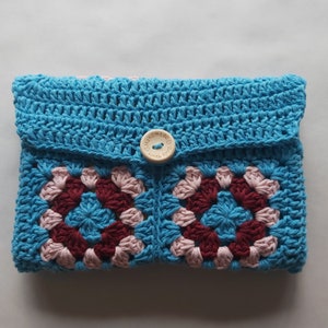 May include: A blue crocheted pouch with a pink and burgundy granny square pattern. The pouch has a wooden button with the text "Handmade with love" on it.