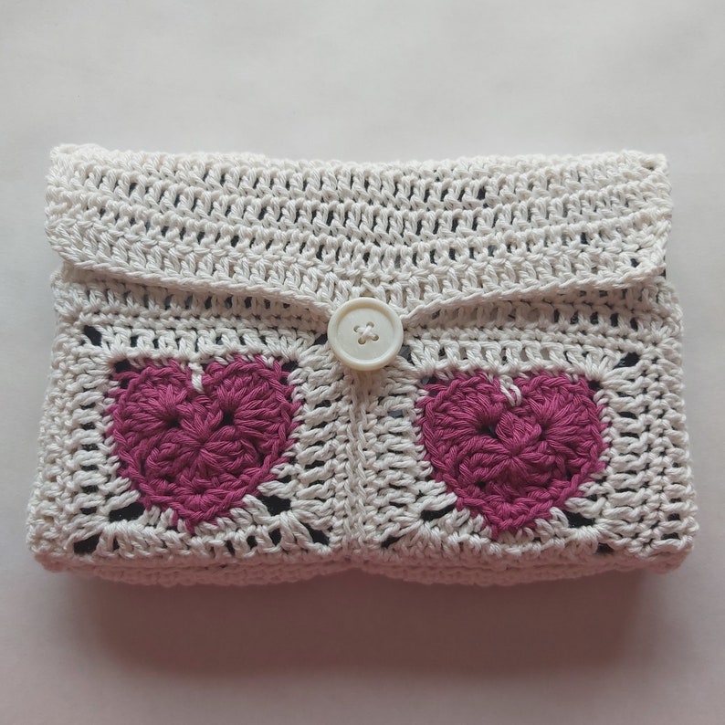 May include: White crocheted clutch with a button closure and two pink crocheted hearts.