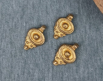 May include: A wooden box with a lid filled with gold-colored metal charms. The box is open and the lid is laying next to it. There are four charms on a blue surface next to the box.