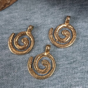 Puede incluir: Tres abalorios de metal de color dorado en forma de espiral. Los abalorios están sobre un fondo de tela azul.