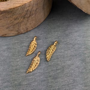 Puede incluir: Tres abalorios de hoja de oro con una superficie texturizada. Los abalorios están sobre un fondo de tela gris.