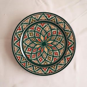 May include: A green ceramic plate with a colourful geometric pattern. The pattern features red, orange, yellow, and green colours. The plate has a white background.