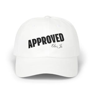 May include: A white baseball cap featuring the word "APPROVED" in bold, black capital letters. Beneath, the phrase "As Is" is written in a smaller, cursive font. The cap has a curved peak and a button on top. A casual accessory.
