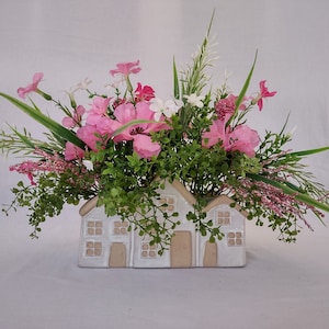 Pink and white faux floral centerpiece in a ceramic beige and white vase that  three house attached house fronts.