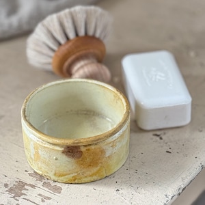 May include: A yellow ceramic bowl with brown and white marbling. The bowl is empty and has a smooth, rounded interior.