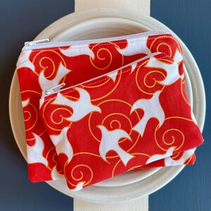 May include: Two red zippered pouches with a white and gold swirling pattern. The pouches are made of fabric and have a zipper closure.