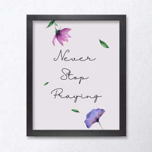 Puede incluir: Una impresión enmarcada con fondo blanco y marco negro. La impresión presenta una ilustración de acuarela de flores moradas y hojas verdes. El texto "Never Stop Praying" está escrito en cursiva negra.