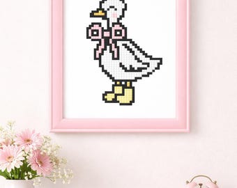 May include: A framed cross-stitch of a white duck wearing yellow boots and a pink bow. The duck is pixelated, with a yellow beak and black details. The frame is pink, and the image is displayed on a white wall.