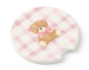 May include: Round car coaster with a pink and white gingham pattern. A watercolor illustration of a brown teddy bear with pink bows is centered on the coaster. The coaster has a small notch for easy removal from the car cup holder.